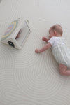 A baby lying on a white floor, playing with a colorful toy beside them.