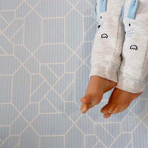 Kid laying on Forrest Baby Blue playmat. Side A has a geometric pattern.