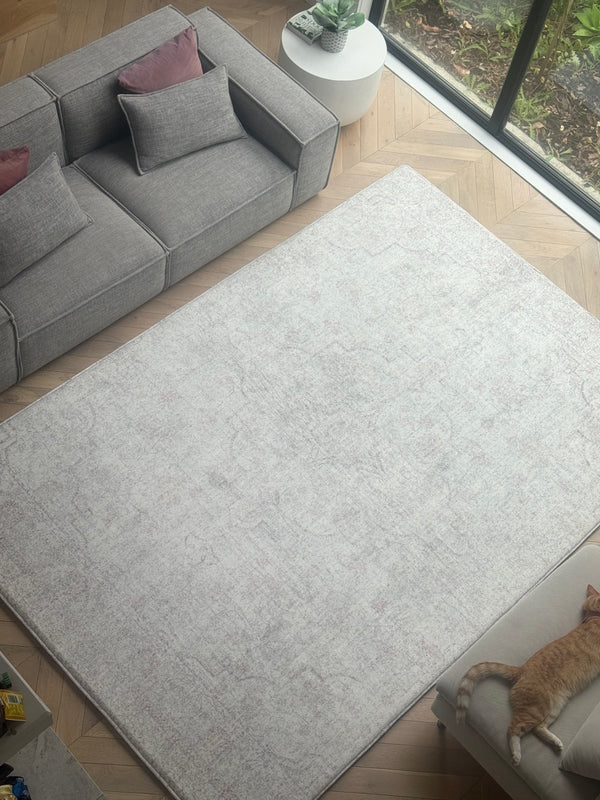 Light gray rug with a distressed texture, placed in a room with a gray sectional sofa and wooden floors.