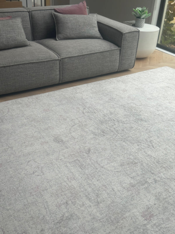 Light gray rug with a distressed texture, placed in a room with a gray sectional sofa and wooden floors.