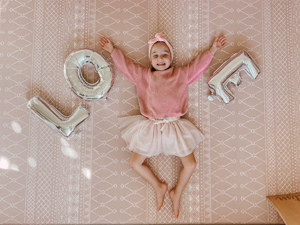 A little girl in pink and white holds a large silver balloon that reads "love," smiling joyfully.