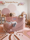 A child sits in a dusty rose crescent-shaped sensory lounge chair, reading a book with their back to the camera in a styled nursery setting.