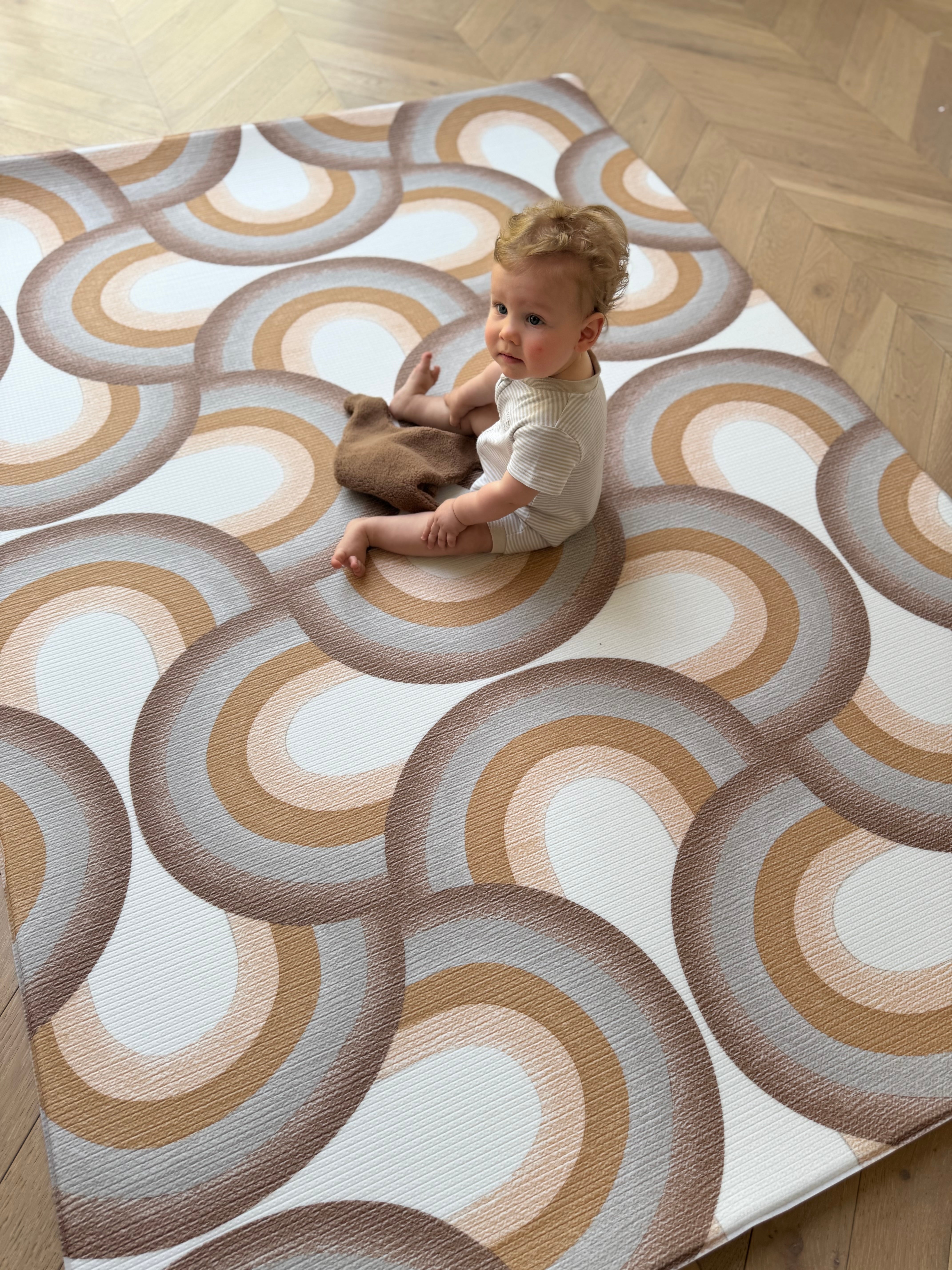 A baby sits on a patterned rug, engaging with a fluffy stuffed animal, surrounded by a cozy atmosphere.