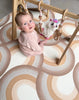 Baby girl playing with a wooden gym, while sitting on Archie Retro Large playmat.