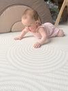 Baby girl doing tummy time on Archie Retro Large playmat. Side B has a white arch pattern.