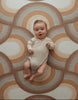 Baby laying on Archie Retro playmat. The playmat has a brown rainbow pattern.