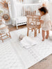 Girl playing in her nursery, standing on the Baby Driver Boho playmat. Side A has a neutral boho pattern.