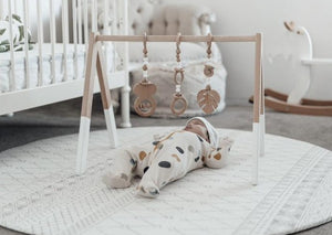 Baby playing with wooden gym on the Baby Driver Boho Round playmat. Side A has a neutral boho pattern.