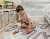 Kid playing with wooden toys on Baby Driver Grey Boho round playmat. Side B has a car track design.