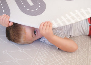 Kid playing with Baby Driver Grey Boho round playmat. Side A has a Neutral boho pattern and side B has a car track design.