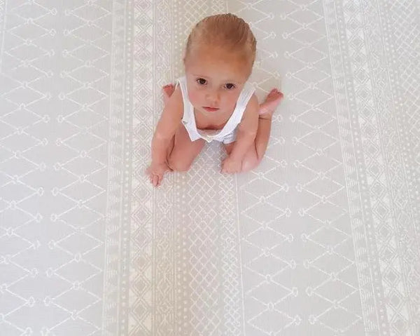 Girl sitting on Boho Boho Grey playmat. Side A has a neutral boho pattern.
