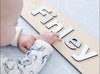 Baby with name sign on Forrest Baby Blue playmat. Side A has a blue geometric pattern.