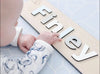 Baby with name sign on Forrest Baby Blue playmat. Side A has a blue geometric pattern.