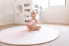 Kid playing on Forrest Blush Round playmat. Side A has a pink geometric pattern.