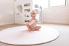 Kid playing on Forrest Blush Round playmat. Side A has a pink geometric pattern.