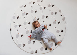 Kid laying on Forrest Grey Round playmat. Side B has a tree and bear pattern. 