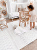 Kid playing in her nursery and standing on Boho Boho Grey playmat. Side A has a neutral boho pattern.